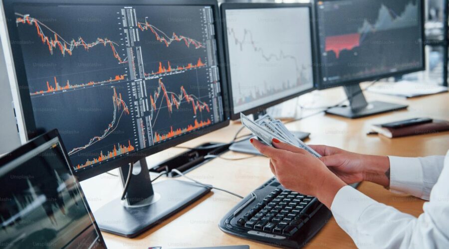 Close up view of woman's hands that holds money near the monitors with graphs.